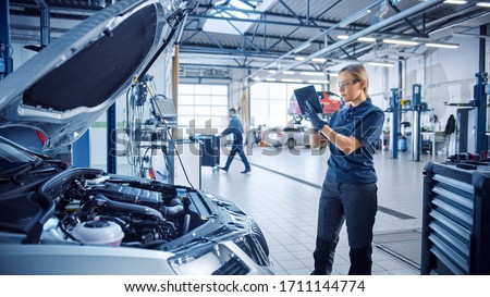 Female Mechanic Uses a Tablet Computer with an Augmented Reality Diagnostics Software. Specialist Inspecting the Car in Order to Find Broken Components Inside the Engine Bay. Modern Car Service. Foto stock © 