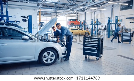Two Mechanics in a Service are Inspecting a Car After They Got the Diagnostics Results. Female Specialist is Comparing the Data on a Tablet Computer. Repairman is Using a Ratchet to Repair the Faults. Foto stock © 