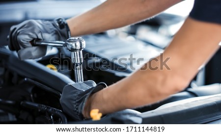Close Up Shot of a Professional Mechanic Working on Vehicle in Car Service. Engine Specialist Fixing Motor. Repairman is Wearing Gloves and Using a Ratchet. Modern Clean Workshop. Foto stock © 