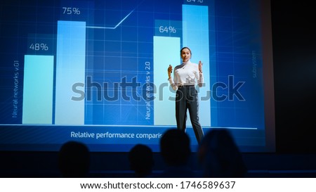 On Stage, Successful Female Speaker Presents Technological Product, Uses Remote Control for Presentation, Showing Infographics, Statistics Animation on Screen. Live Event  Device Release.