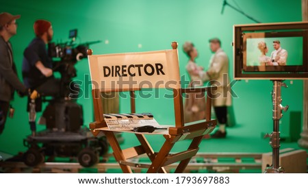 On Film Studio Set Focus on Empty Director's Chair. In the Background Professional Crew Shooting Historic Movie, Cameraman on Railway Trolley Shooting Green Screen Scene with Actors for History Movie