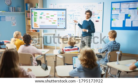 Elementary School Computer Science Teacher Uses Interactive Digital Whiteboard to Show Programming Logics to a Classroom full of Smart Diverse Children. Computer Class with Kids Listening