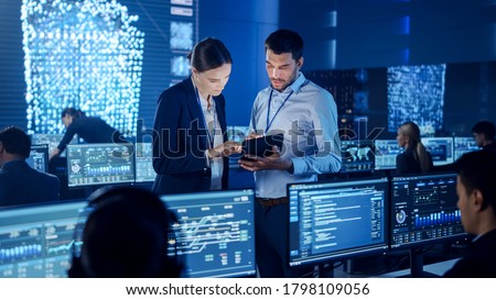 Project Manager and Computer Science Engineer Talking while Using A Digital Tablet Computer. Telecommunications Company System Control and Monitoring Office Room with Working Specialists.