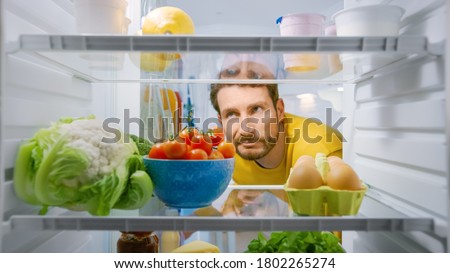 Inside Kitchen Fridge: Young Disappointed Man Looks inside the Fridge. Man Found Nothing for His Snack Time. Point of View POV Shot from Refrigerator full of Healthy Food