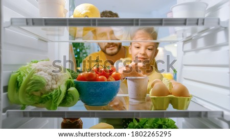 Camera Inside Kitchen Fridge: Dad Lifts Cute Little Daughter to Choose Whatever She wants to Take From the Fridge, She Chooses Healthy Yogurt. Point of View POV Shot from Refrigerator full of Food