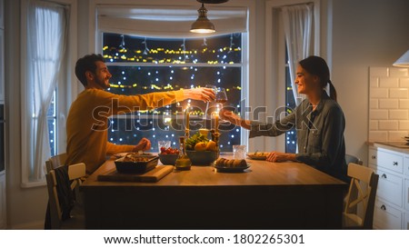 Happy Young Couple in Love Have Romantic Dinner, Toasting Each other with Glasses of Wine, Eating Tasty Meal in the Kitchen, Celebrating, Talking. Beautiful Lovely Husband and Wife Have Romantic Time