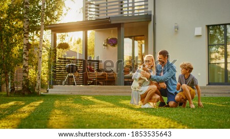 Smiling Father, Mother and Son Pet and Play with Smooth Fox Terrier Retriever Dog. Sun Shines on Idyllic Happy Family with Loyal Pedigree Dog have Fun at the Idyllic Suburban House Backyard
