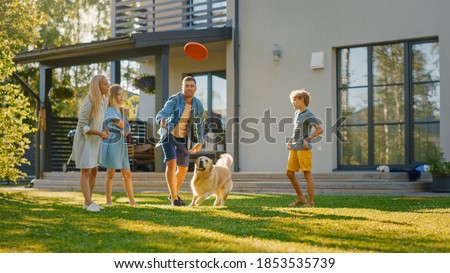 Smiling Beautiful Family of Four Play Fetch flying disc with Happy Golden Retriever Dog on the Backyard Lawn. Idyllic Family Has Fun with Loyal Pedigree Dog Outdoors in Summer House Backyard