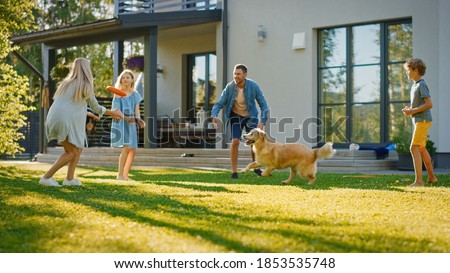 Smiling Beautiful Family of Four Play Fetch flying disc with Happy Golden Retriever Dog on the Backyard Lawn. Idyllic Family Has Fun with Loyal Pedigree Dog Outdoors in Summer House Backyard Foto stock © 