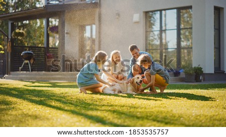 Beautiful Smiling Family of Four Cuddling Happy Golden Retriever Dog on the Backyard Lawn. Idyllic Family Cuddling Loyal Pedigree Dog Outdoors in Summer House Backyard.