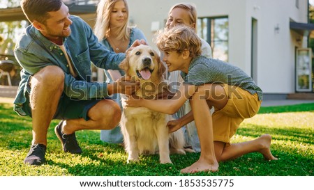 Smiling Beautiful Family of Four Posing with Happy Golden Retriever Dog on the Backyard Lawn. Idyllic Family Cuddling Loyal Pedigree Dog Outdoors in Summer House Backyard.
