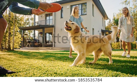Smiling Beautiful Family of Four Play Catch flying disc with Happy Golden Retriever Dog on the Backyard Lawn. Idyllic Family Has Fun with Loyal Pedigree Dog Outdoors in Summer House.