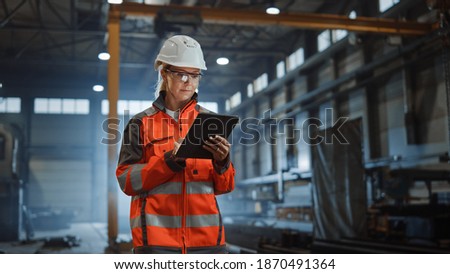 Professional Heavy Industry Engineer Worker Wearing Safety Uniform and Hard Hat, Using Tablet Computer. Serious Successful Female Industrial Specialist Walking in a Metal Manufacture Warehouse. Foto d'archivio © 