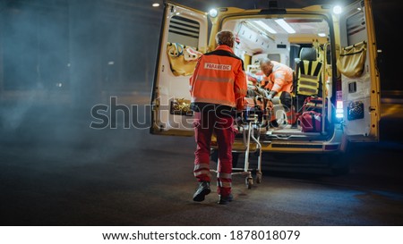Team of EMS Paramedics React Quick to Provide Medical Help to Injured Patient and Get Him in Ambulance on a Stretcher. Emergency Care Assistants Arrived on the Scene of a Traffic Accident on a Street. Blur