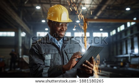 Professional Heavy Industry Engineer Worker Wearing Safety Uniform and Hard Hat Uses Tablet Computer. Smiling African American Industrial Specialist Standing in a Metal Construction Manufacture. 商業照片 © 