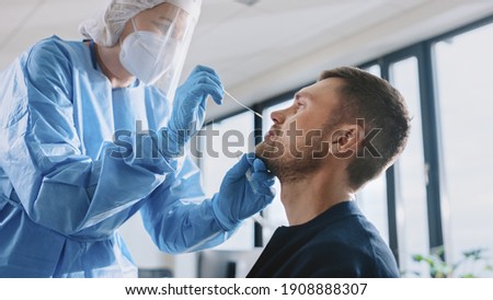 Medical Nurse in Safety Gloves and Mask, Protective Face Shield and Overalls is Taking a PCR Corona Virus Sample in a Health Clinic. Doctor Uses Respiratory Swab Test. Covid-19 Pandemic Concept.
