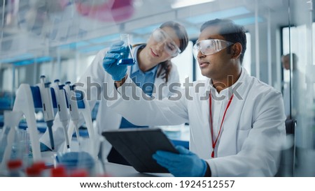 Modern Medical Research Laboratory: Two Scientists Working Together Analysing Chemicals in Laboratory Flask, Discussing Problem. Advanced Scientific Lab for Medicine, Biotechnology, Molecular Biology