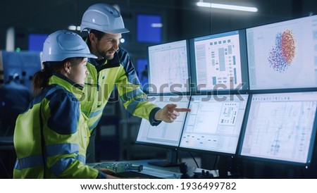Industry 4.0 Modern Factory: Chief Project Manager Talks to Female Engineer, She Points at Computer Screens Showing Complex Industrial Electronics Design Blueprints, They Have Find Problem Solution