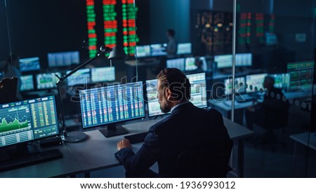 Professional Financial Data Analysts Working in a Modern Monitoring Office with Live Analytics Feed on a Big Digital Screen. Monitoring Room with Finance Specialists Sit in Front of Computers.
