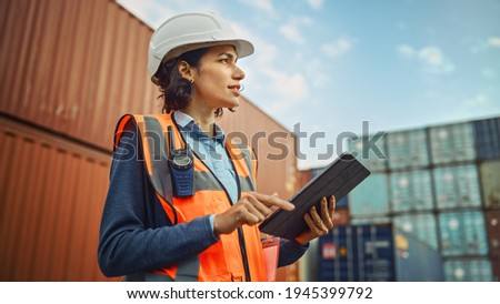 Smiling Portrait of a Beautiful Latin Female Industrial Engineer in White Hard Hat, High-Visibility Vest Working on Tablet Computer. Inspector or Safety Supervisor in Container Terminal. Stockfoto © 