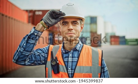 Smiling Portrait of a Handsome Caucasian Industrial Engineer in White Hard Hat, Orange High-Visibility Vest, Checkered Shirt and Work Gloves. Foreman or Supervisor Has a Two-Way Radio Attached. Foto stock © 