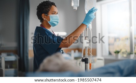 Hospital Ward: Professional Black Head Nurse Wearing Face Mask Does Checkup of Patient's Vitals, Checking Heart Rate Computer, Intravenous or Iv Fluids Drip Bag. Caring Nurse Monitors Person Recovery 商業照片 © 