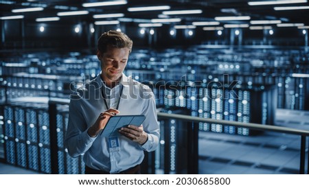 Portrait of Smiling IT Specialist Using Tablet Computer in Data Center. Big Server Farm Cloud Computing Facility with Male Maintenance Administrator Working. Cyber Security, e-Business. Stockfoto © 