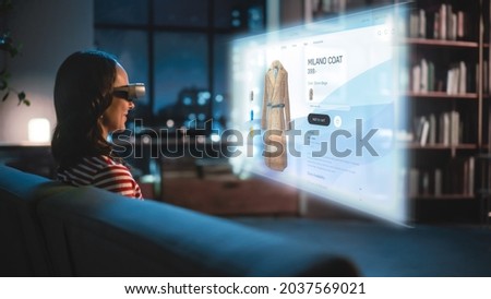 Young Woman Using Virtual Reality Headset At Home, Sitting on a Couch, Shopping Online via VR Clothing Store. Evening Resting at Apartment, Choosing New Look. Over the Shoulder Stok fotoğraf © 