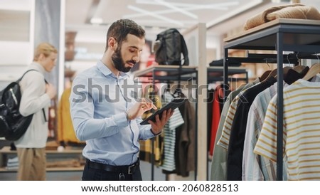 Clothing Store: Male Visual Merchandising Professional Uses Tablet Computer To Create Collection. Fashionable Shop Sales Retail Manager Checks Stock. Small Business Owner Orders Stylish Items 商業照片 © 