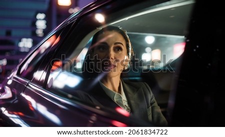 Beautiful Businesswoman is Commuting from Office in a Backseat of Her Luxury Car at Night. Entrepreneur Passenger Traveling in a Transfer Taxi in Urban City Street with Working Neon Signs. Foto stock © 