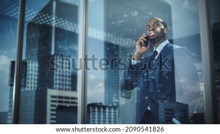 Portrait of Successful African-American Businessman Standing in Office, Making Phone Call to Close the Deal, Looking out of Window. Successful Stock Market Investor Making e-Business. Outside Shot Imagine de stoc © 