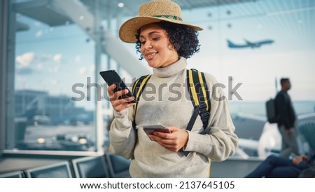 Airport Terminal: Happy Traveling Black Woman Waiting at Flight Gates for Plane Boarding, Uses Mobile Smartphone, Checking Trip Destination on Internet. Smiling African American Female on Vacation Foto stock © 