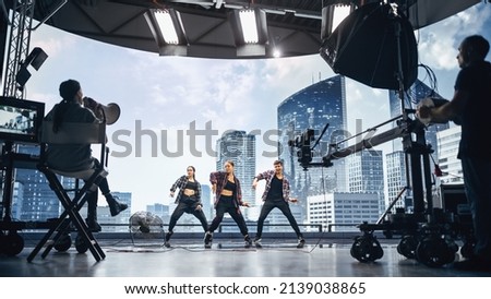 Music Clip Studio Set: Shooting Hip Hop Video Dance Scene with Three Professionals Dancers Performing on Stage with Big Led Screen with Modern City Background. Director and Cameraman in Backstage. Сток-фото © 