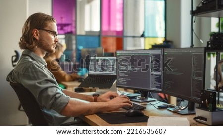 Young Caucasian Man Coding on Personal Computer and Laptop Set Up In Stylish Office. Professional Programmer Developing Innovative AI Software in Technological Start-Up, Using Multiple Displays. Foto d'archivio © 