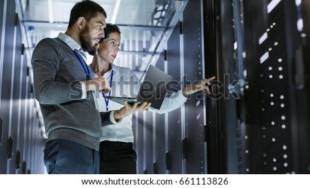 Male IT Specialist Holds Laptop and Discusses Work with Female Server Technician. They're Standing in Data Center, Rack Server Cabinet is Open. ストックフォト © 