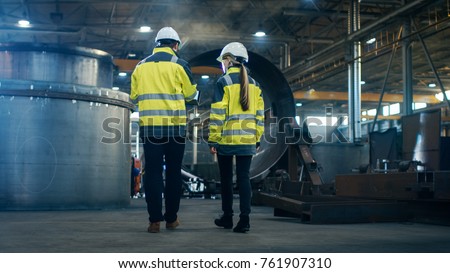 Male and Female Industrial Engineers use Laptop and Have Discussion While Walking Through Heavy Industry Manufacturing Factory. They Wear Hard Hats and Safety Jackets. 商業照片 © 