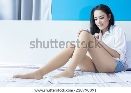 smiling young woman using and touching cell phone on the bed