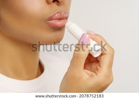 African woman applying balsam lipstick to moisturize lips and protect from cold and wind. Unrecognizable black female using natural hygienic balm for skin protection and skincare, closeup cropped shot Foto stock © 