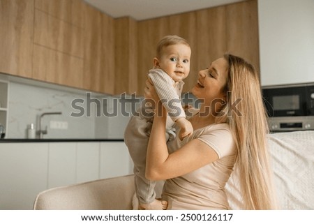 Similar – Foto Bild Blonde Mutter hält ihr bezauberndes fröhliches kleines Baby im Arm. Nettes Kleinkind Kind in die Kamera schauen und lächelnd zu Hause