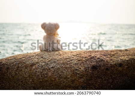 Lonely Alone Bear sitting on Stone with Sea Overlight Background,Poster Abandoned Baby Symbols,Teddy Child at Coast Water Nature,Vintage  Photography,Card Love Valentine Day or Broken Heart Concept. Stock foto © 