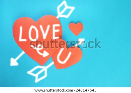 Writing Love you and arrow on red hearts paper on cyan paper background for Valentines day