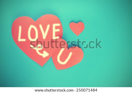 Writing Love you on red hearts paper on cyan paper background for Valentines day - vintage tone