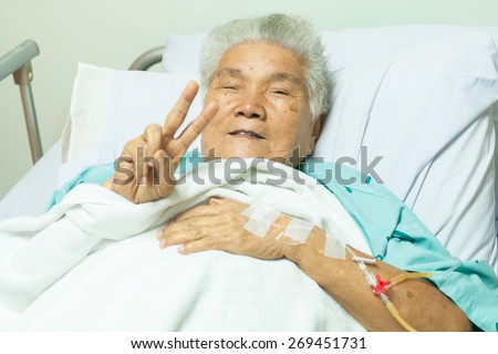 Happy senior female patient making finger victory sign for cheerful in bed at hospital