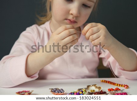 Pretty little girl threading beads and making bracelet