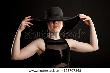 Beautiful girl in a black hat, black background