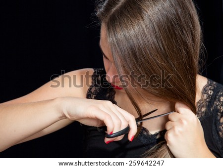 Portrait of a sad young woman clipping her long hair, black background