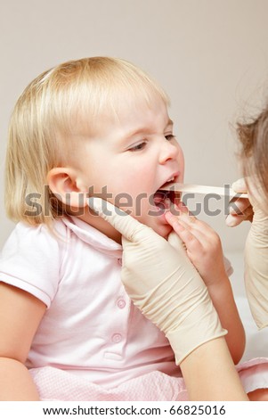 Pediatrician examining little girl\'s throat with tongue depressor