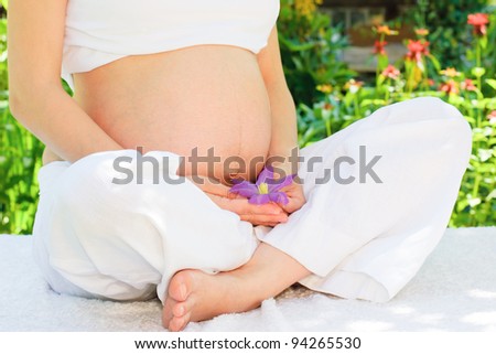 Young pregnant woman relaxing in a summer garden holding Clematis flower