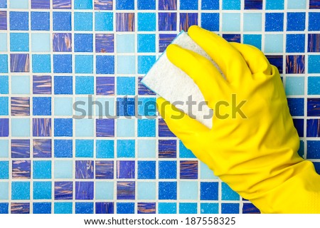 Hand in yellow protective glove cleaning mosaic wall with sponge