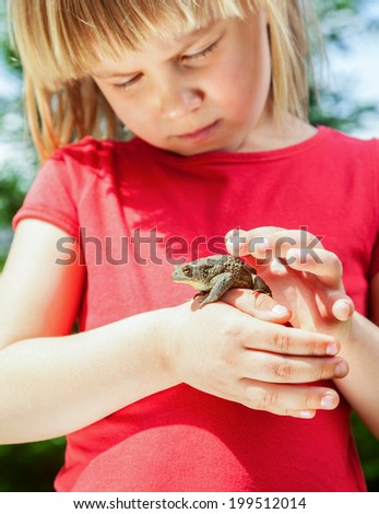 Little girl looking at true toad sitting on her hand